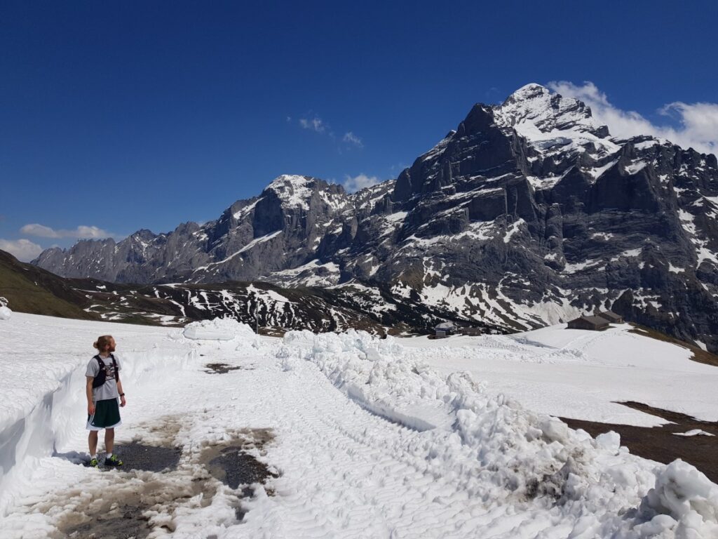 Man standing in a lot of snow in June in Grindelwald Switzerland looking at the Wetterhorn
